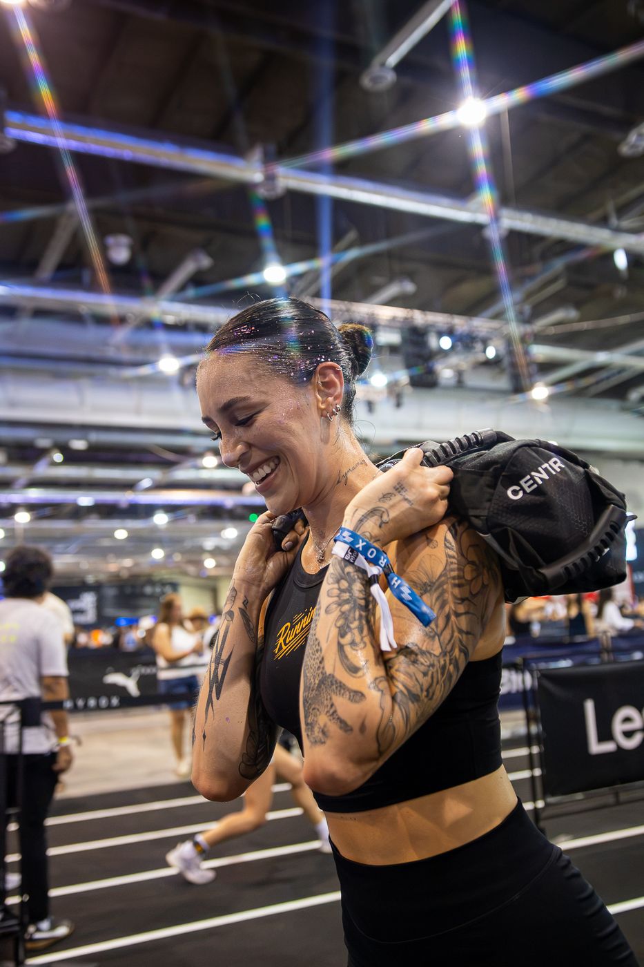 Atleta con tatuajes sonriendo mientras carga el costal de arena en HYROX